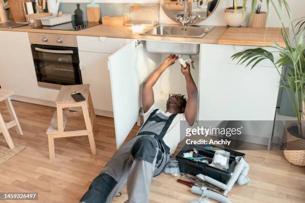 plumber working on pipes under sink - under sink stock pictures, royalty-free photos & images