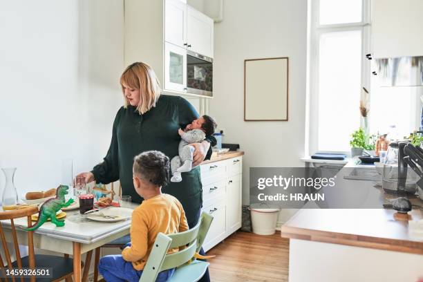 mother carrying newborn baby and serving food to son in kitchen - newborn sibling stock pictures, royalty-free photos & images