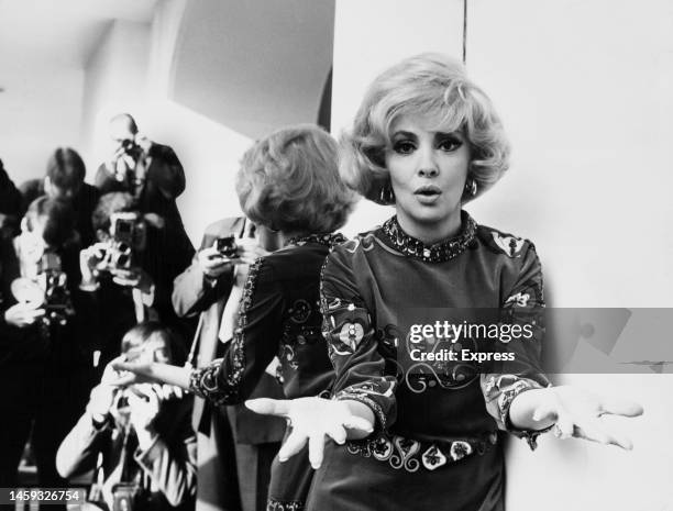 Press photographers are reflected in a mirror as Italian actress Gina Lollobrigida poses wearing a blonde wig during a press call at the Savoy Hotel,...