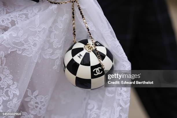 Guest wears a white lace print pattern ruffled long skirt from Chanel, a black and white checkered print pattern ball handbag from Chanel , outside...