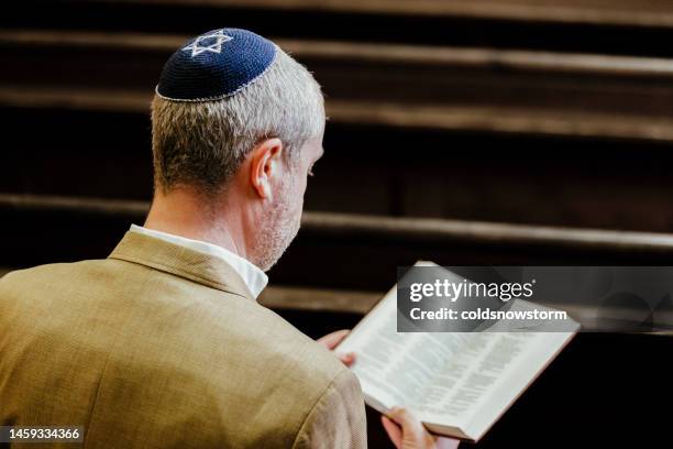 jewish man wearing yarmulke while reading holy book in synagogue - jewish people stockfoto's en -beelden