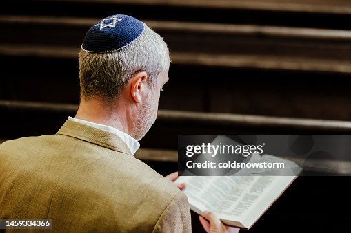 Jewish man wearing yarmulke while reading holy book in synagogue