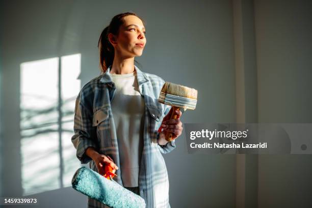 a young joyful woman stands with a roller and a brush - paint preparation stock pictures, royalty-free photos & images