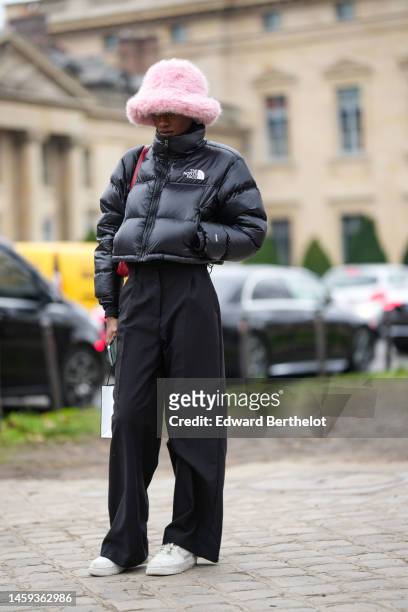 Guest wears a pale pink fluffy oversized hat, a black shiny high neck cropped puffer jacket from The North Face, high waist black wide legs pants, a...