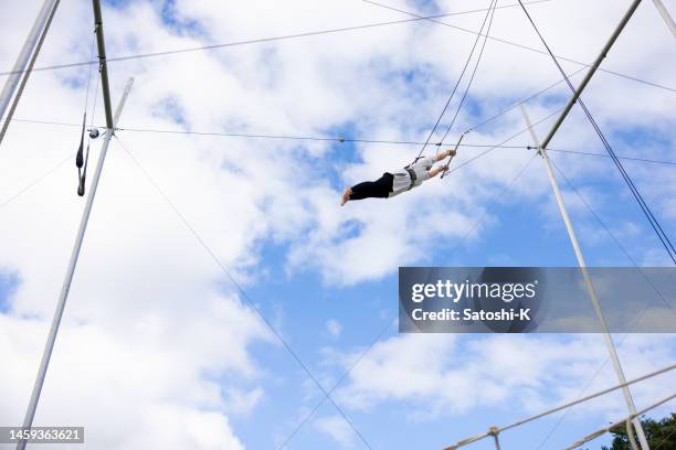 青空を飛ぶ成熟した空中ブランコアーティスト - trapeze ストックフォトと画像