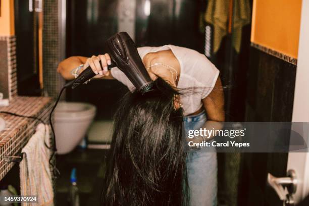 young woman in bathroom using hairdryer - blow drying hair stock-fotos und bilder