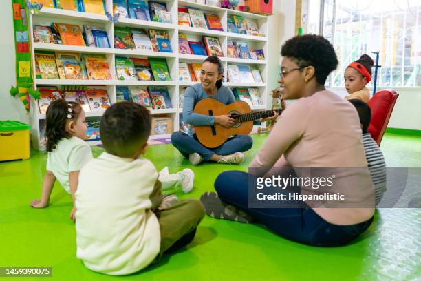 enfants chantant des chansons en classe de musique et enseignant jouant de la guitare - enfant chant classe photos et images de collection
