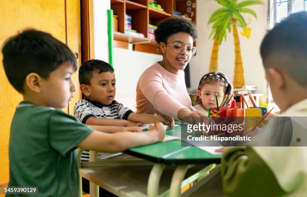 arts teacher supervising a group of kids coloring in class - preschool age stockfoto's en -beelden