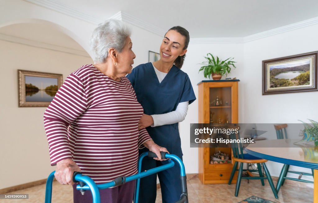 Häusliche Pflegekraft hilft einer älteren Frau, die einen Rollator zu Hause benutzt