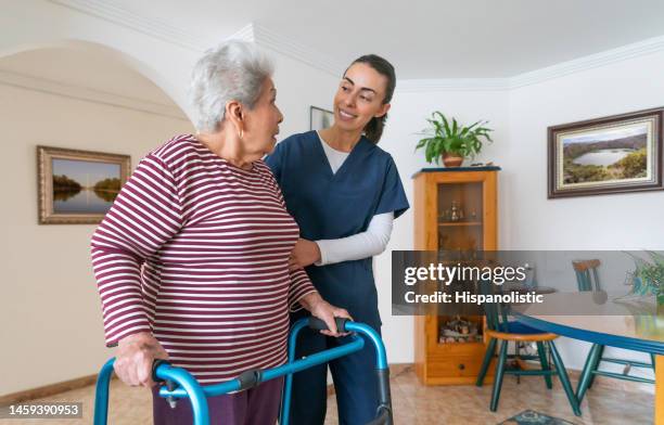 assistente domiciliare che aiuta una donna anziana usando un deambulatore a casa - ospizio foto e immagini stock