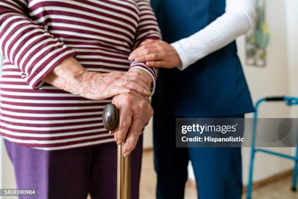 senior woman walking with a cane with the help of her caregiver - retirement community staff stock pictures, royalty-free photos & images