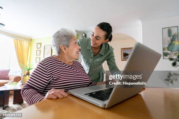 young woman helping a senior woman paying her bills online - grandma invoice stock pictures, royalty-free photos & images