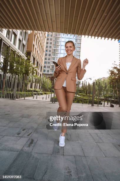 adult elegant businesswoman wearing beige pantsuit walking outdoors - russian business woman stock-fotos und bilder