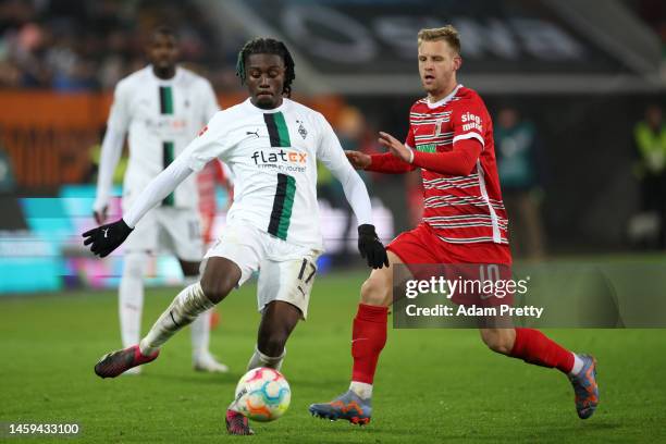 Kouadio Kone of Borussia Monchengladbach is challenged by Arne Maier of FC Augsburg during the Bundesliga match between FC Augsburg and Borussia...