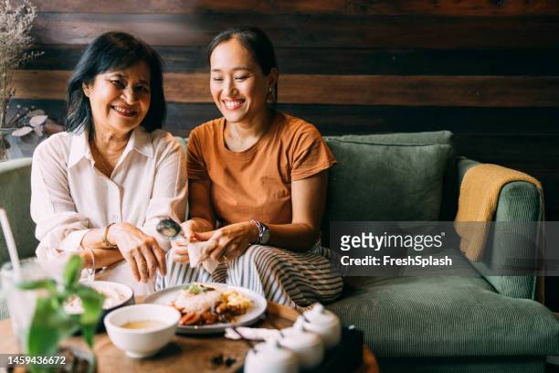 ein porträt einer glücklichen, schönen älteren frau, die in die kamera schaut, während sie mit ihrer hübschen tochter im restaurant sitzt - asian restaurant stock-fotos und bilder