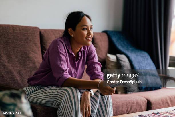 a happy beautiful woman watching tv while relaxing at home - alter tv stock pictures, royalty-free photos & images