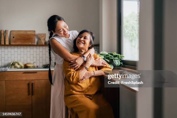 una bella donna felice che abbraccia sua madre mentre è seduta in cucina e beve il tè - embracing foto e immagini stock