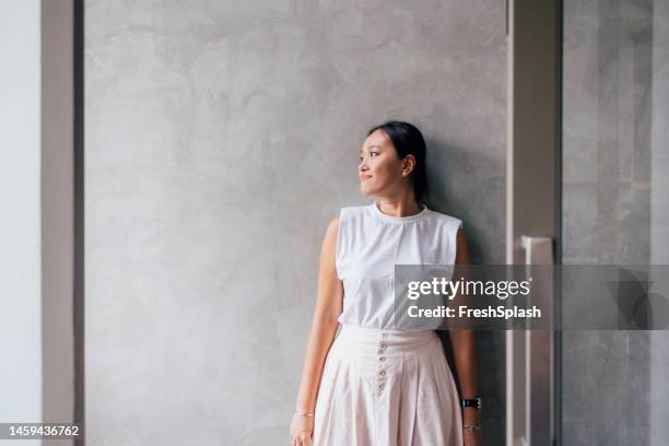 a happy beautiful woman looking away while standing against grey background - women standing against grey background stock pictures, royalty-free photos & images