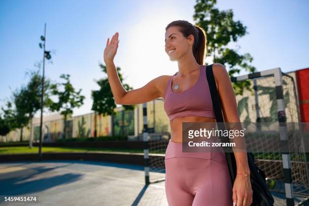 happy woman in sports clothing arriving at public sports field with bag on shoulder, waving at friends - serbia handball stock pictures, royalty-free photos & images