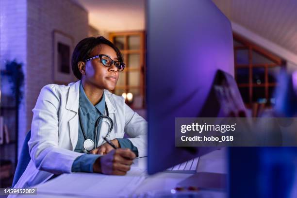 mid adult female doctor filling papper forms and working using computer late at night - ehealth stockfoto's en -beelden