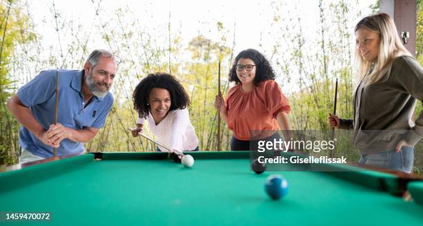 mujer joven jugando al billar con su padre y amigos afuera en un patio - pool table fotografías e imágenes de stock