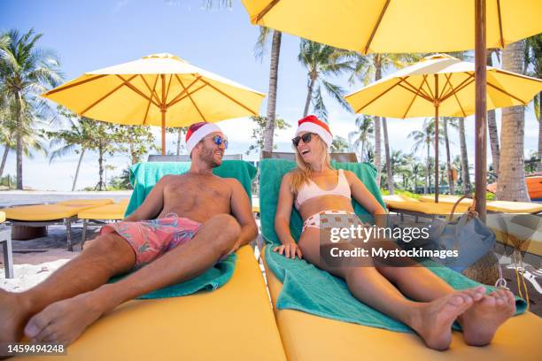 tourist couple on christmas resort vacation sunbathing wearing santa hats - christmas travel stock pictures, royalty-free photos & images