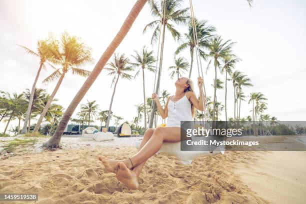 playful young woman on tropical beach using swing at sunrise - vietnam strand stock pictures, royalty-free photos & images