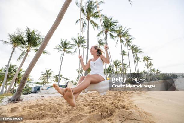 giovane donna giocosa sulla spiaggia tropicale usando l'altalena all'alba - fare laltalena foto e immagini stock