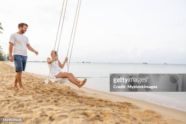 playful young couple on tropical beach using swings at sunrise - vietnam beach stockfoto's en -beelden