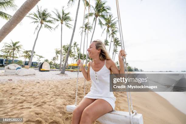 giovane donna giocosa sulla spiaggia tropicale usando l'altalena all'alba - fare laltalena foto e immagini stock