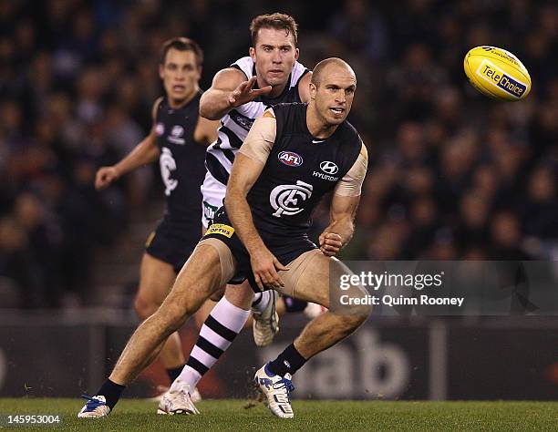 Chris Judd of the Blues handballs whilst being tackled by Orren Stephenson of the Cats during the round 11 AFL match between the Carlton Blues and...