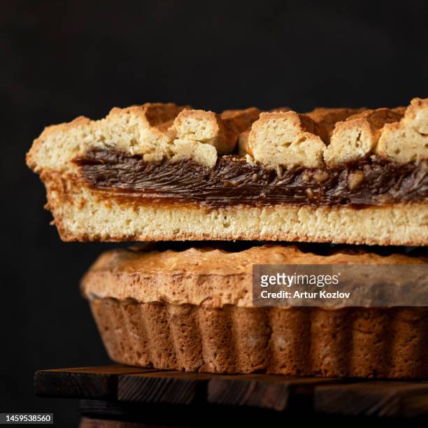 american pie with chocolate filling and mesh top. homemade holiday pastries for family tea drinking. sand cake. dessert in cut form on wooden table. dark background. close-up. side view - chocolate top view stock-fotos und bilder