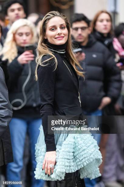 Olivia Palermo wears a black turtleneck wool pullover, a black sleeveless blazer jacket, diamonds necklaces, a long silver chain necklace, rings,...