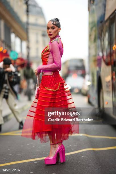 Sira Pevida wears silver earrings, a pink tulle with embroidered red checkered ruffled tulle and gold borders long sleeves / long dress, a gold Knot...