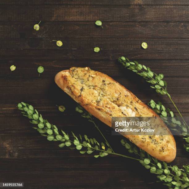 baguette with cheese, garlic and herbs. french and mediterranean cuisine. fresh pastries on wooden background with green plant. view from above. copy space. dark background - garlic bread stock pictures, royalty-free photos & images