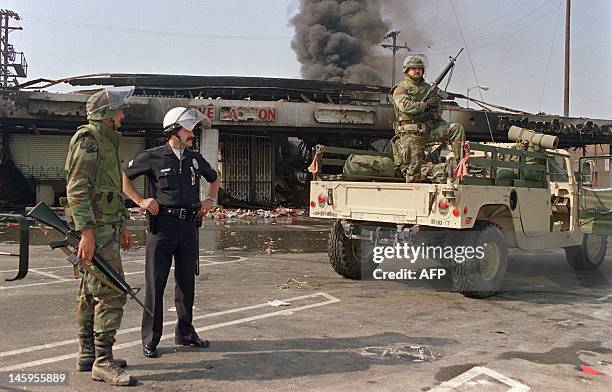 National Guardsmen and a police officer take up security positions in front of a burned and looted shopping center, 01 May 1992 in central Los...