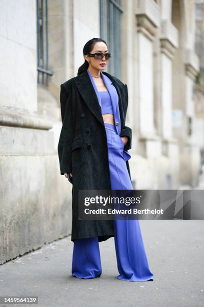 Chriselle Lim wears black sunglasses, earrings, a gold chain with rhinestones necklace from Chanel, a black suede long coat, a purple shoulder-off /...