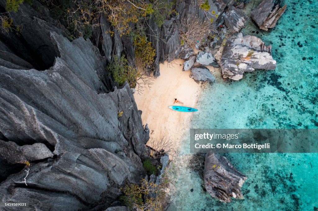 Aerial view of woman with kayak on tiny beach and sharp rock formations, Palawan