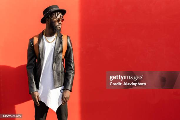 portrait of black man looking into camera with red background on a sunny day - vestimenta 個照片及圖片檔