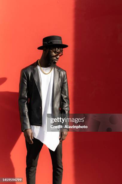 portrait of black man looking into camera with red background on a sunny day - vestimenta stockfoto's en -beelden