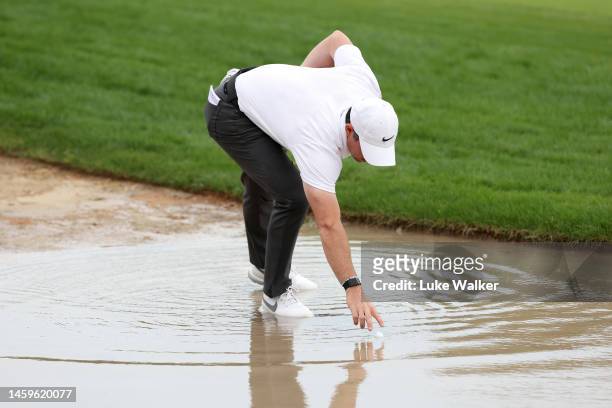 Rory McIlroy of Northern Ireland retrieves their ball from water on the 10th hole during Day One of the Hero Dubai Desert Classic at Emirates Golf...