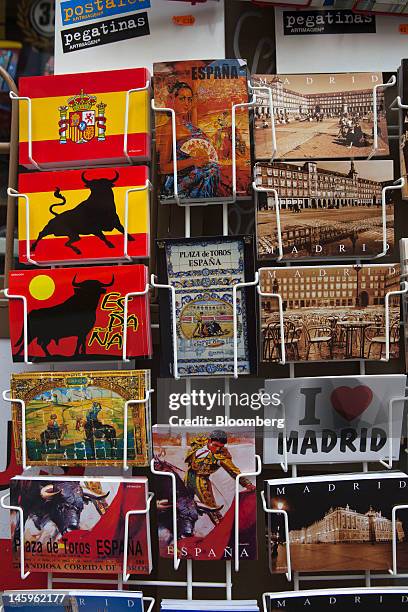 Holiday postcards stand for sale on a rack outside a souvenir store for tourists in Madrid, Spain, on Friday, June 8, 2012. Spain is poised to become...