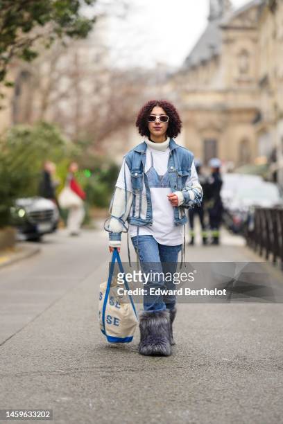Guest wears white sunglasses, a black t-shirt, a white ribbed wool pullover, a white with blue denim bra print pattern a blue denim ripped jacket,...