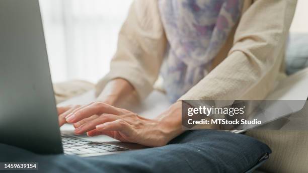 closeup young muslim woman sit on bed with computer laptop and on folding laptop table, portable holder stand hold paperwork and think create on work idea in bedroom at home. work from home. - aanmelden stockfoto's en -beelden