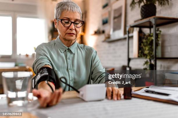 a senior woman measures blood pressure at her home. - hypertension stock-fotos und bilder