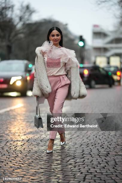 Guest wears a pale pink ruffled tulle t-shirt, a white fur coat, pale pink suit pants, a gray shiny leather Diorama handbag from Dior, silver shiny...