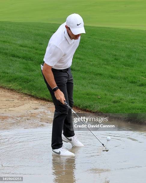 Rory McIlroy of Northern Ireland retrieves his ball from a puddle beside the fairway before he plays his second shot on the 10th hole during Day One...