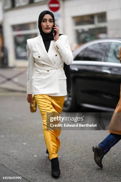 Guest wears a black scarf as a headband, a white latte buttoned / shoulder-pads / blazer jacket, yellow orange shiny satin long skirt, a gold shiny...