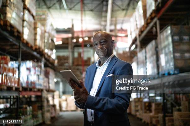 portrait of a mature man using the digital tablet in a warehouse - ceo stock pictures, royalty-free photos & images