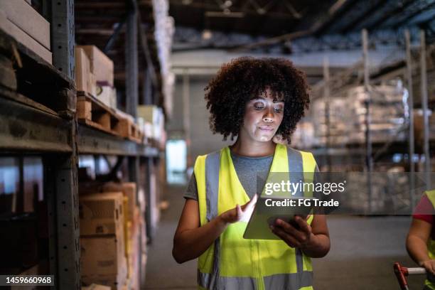 jeune femme utilisant la tablette numérique dans un entrepôt - hangar photos et images de collection